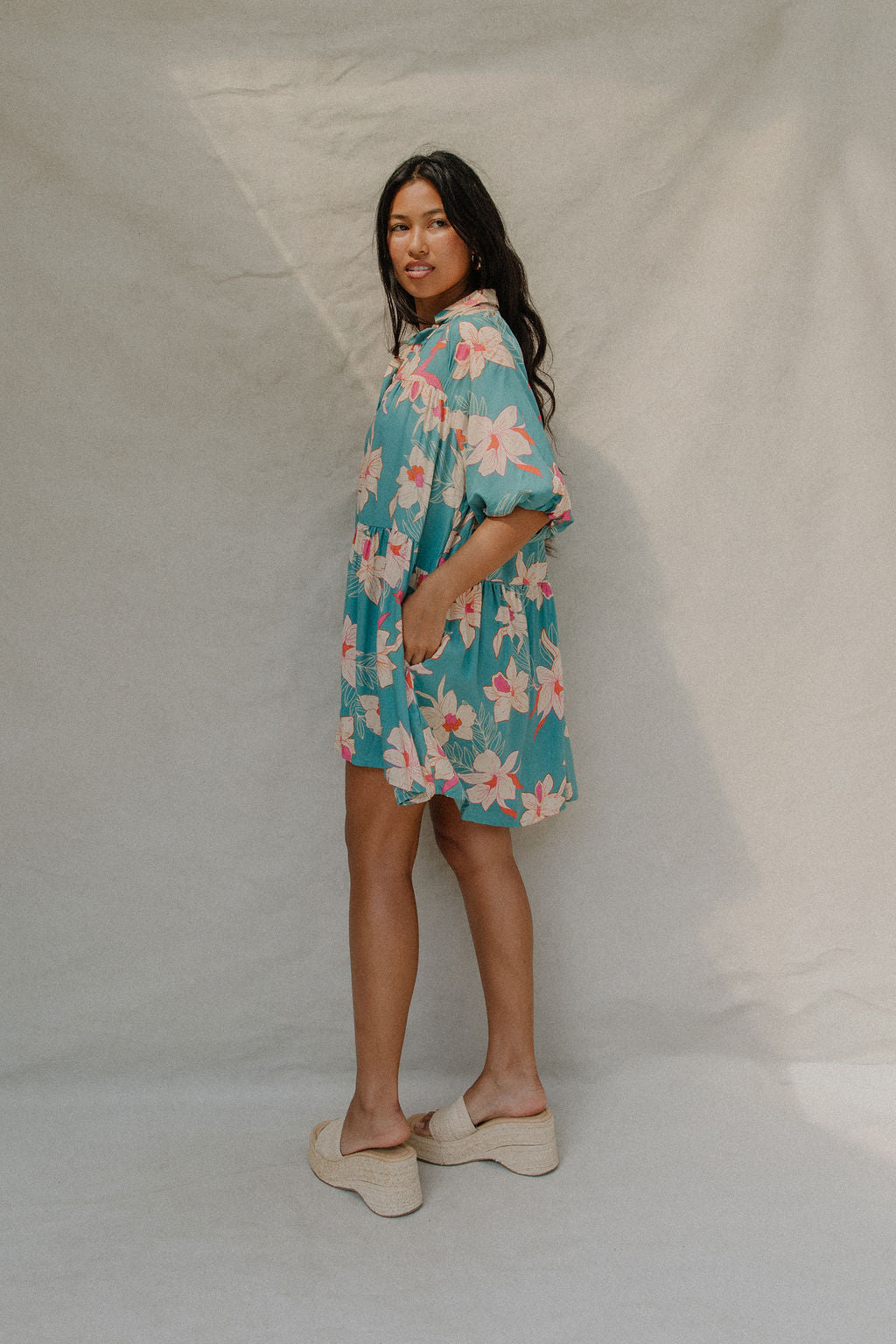 woman with brown hair wearing a teal puff sleeve dress with white orchid pattern