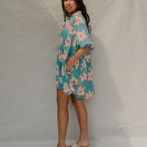 woman with brown hair wearing a teal puff sleeve dress with white orchid pattern