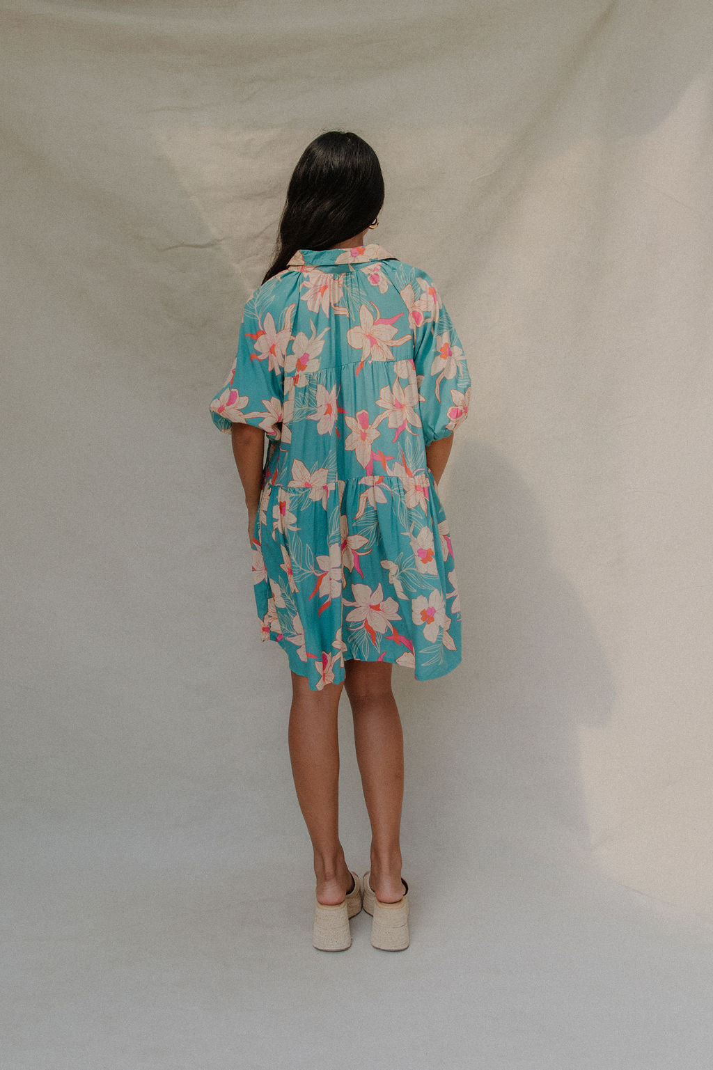woman with brown hair wearing a teal puff sleeve dress with white orchid pattern