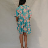 woman with brown hair wearing a teal puff sleeve dress with white orchid pattern
