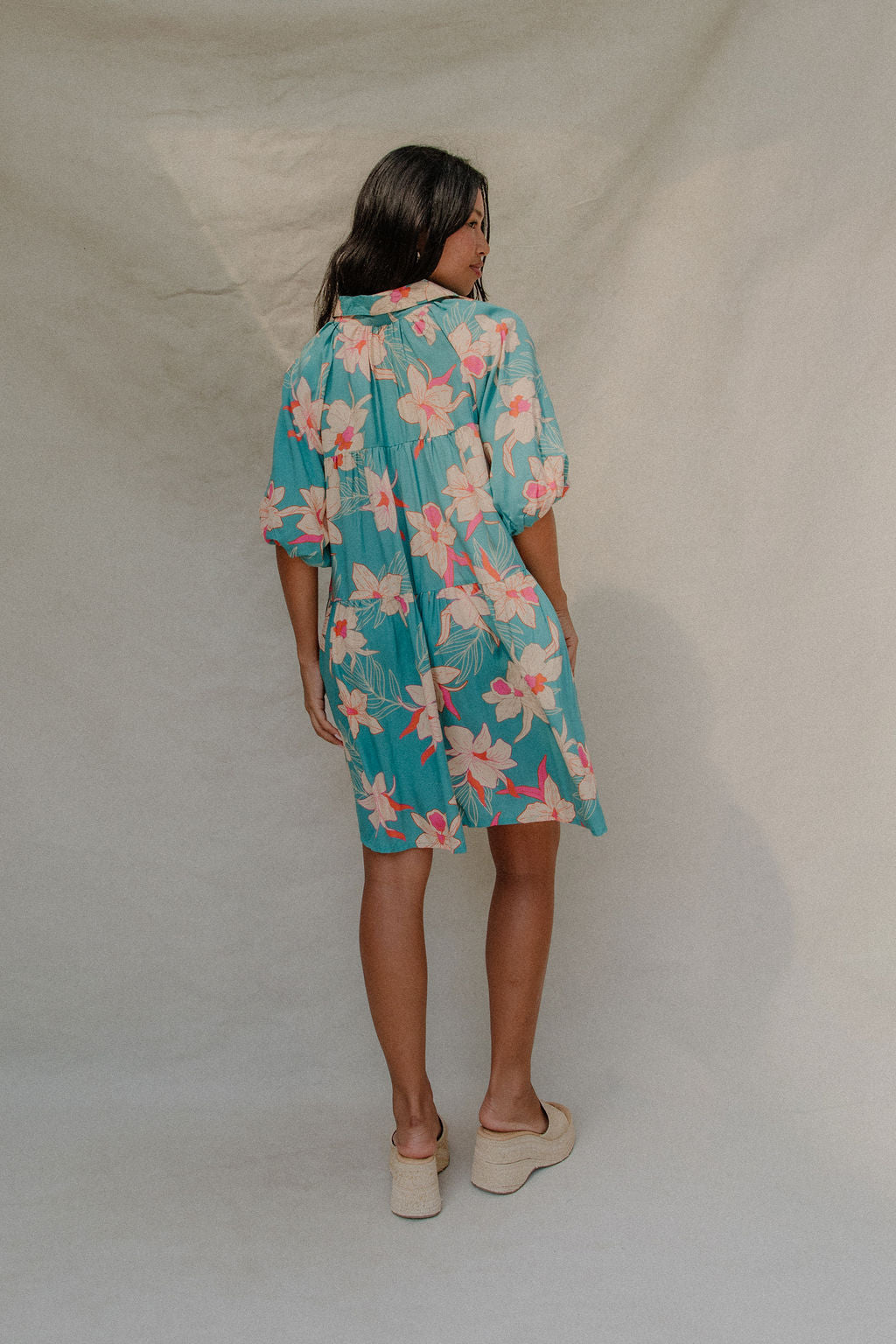 woman with brown hair wearing a teal puff sleeve dress with white orchid pattern