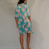 woman with brown hair wearing a teal puff sleeve dress with white orchid pattern