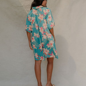 woman with brown hair wearing a teal puff sleeve dress with white orchid pattern