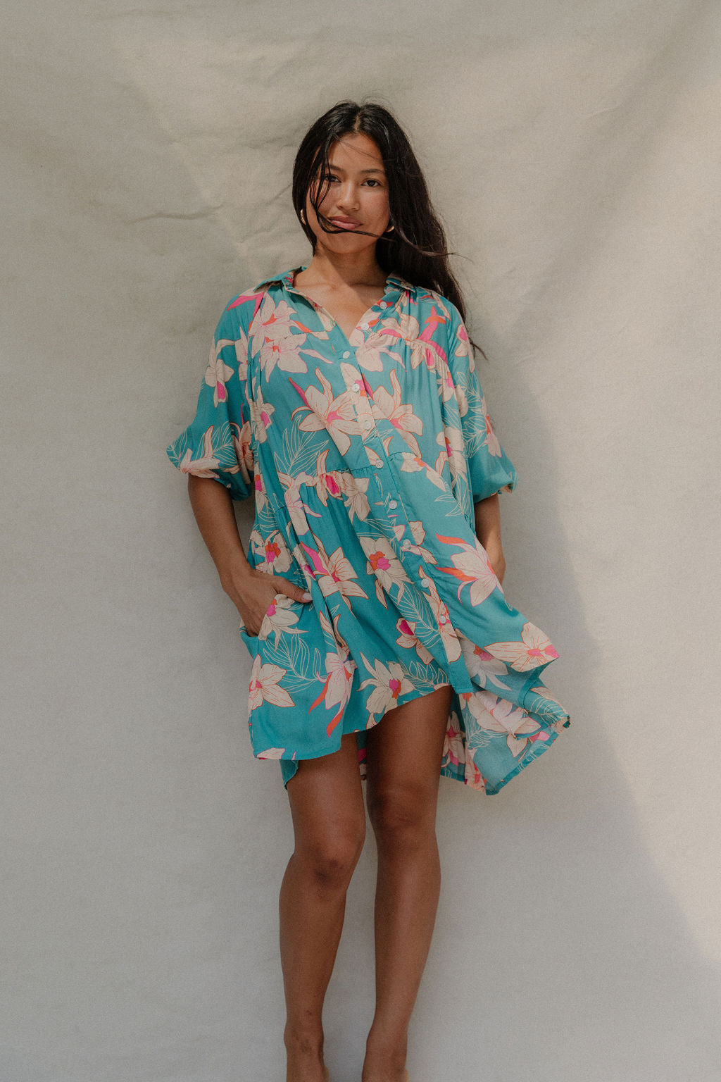 woman with brown hair wearing a teal puff sleeve dress with white orchid pattern