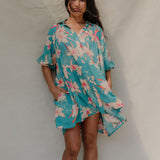 woman with brown hair wearing a teal puff sleeve dress with white orchid pattern