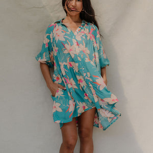woman with brown hair wearing a teal puff sleeve dress with white orchid pattern