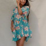 woman with brown hair wearing a teal puff sleeve dress with white orchid pattern