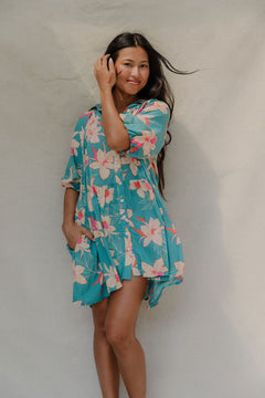 woman with brown hair wearing a teal puff sleeve dress with white orchid pattern