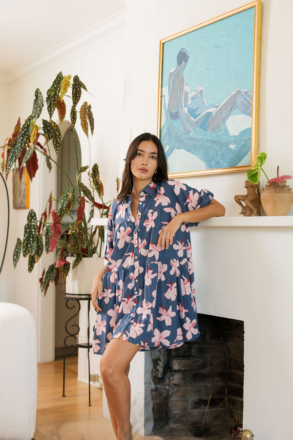 woman with black hair wearing a mini baby doll button up dress in a navy color with pink hibiscus blossoms 