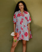 Woman in flowy short sleeve tiered shirt dress with large red and pink floral print on lavender ground.