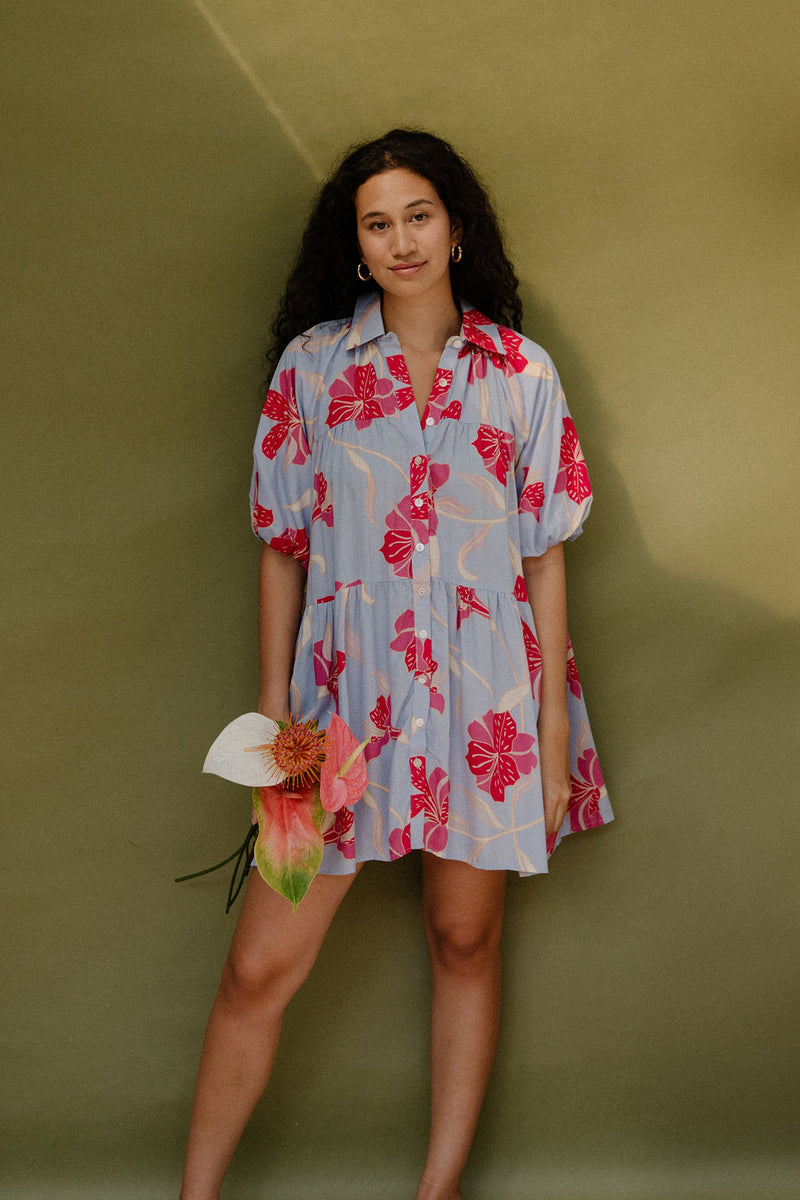 Woman in flowy short sleeve tiered shirt dress with large red and pink floral print on lavender ground.