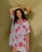 Woman in flowy short sleeve tiered shirt dress with large red and pink floral print on lavender ground.