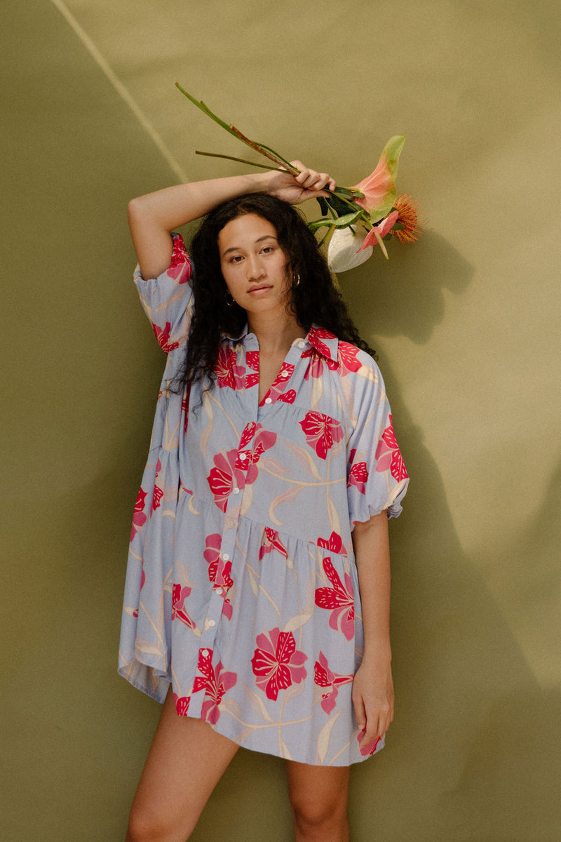 Woman in flowy short sleeve tiered shirt dress with large red and pink floral print on lavender ground.