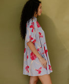 Woman in flowy short sleeve tiered shirt dress with large red and pink floral print on lavender ground.