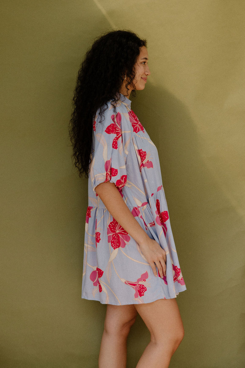 Woman in flowy short sleeve tiered shirt dress with large red and pink floral print on lavender ground.