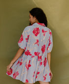 Woman in flowy short sleeve tiered shirt dress with large red and pink floral print on lavender ground.