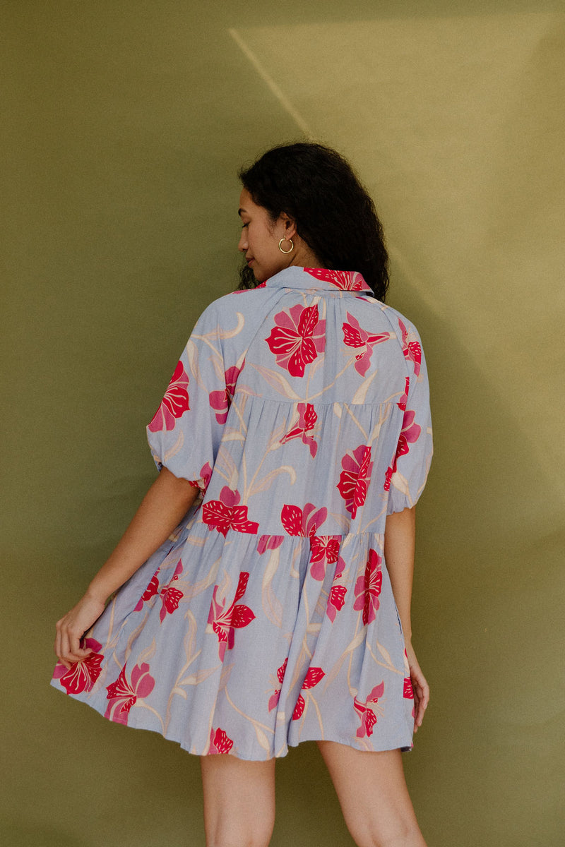 Woman in flowy short sleeve tiered shirt dress with large red and pink floral print on lavender ground.