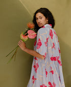 Woman in flowy short sleeve tiered shirt dress with large red and pink floral print on lavender ground.