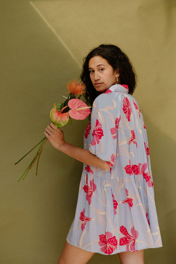 Woman in flowy short sleeve tiered shirt dress with large red and pink floral print on lavender ground.