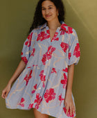 Woman in flowy short sleeve tiered shirt dress with large red and pink floral print on lavender ground.