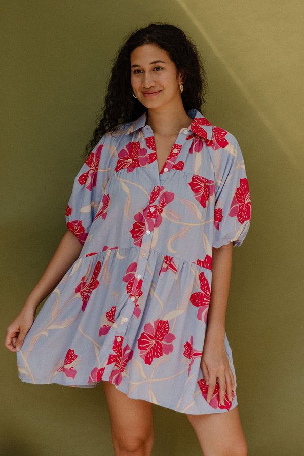 Woman in flowy short sleeve tiered shirt dress with large red and pink floral print on lavender ground.