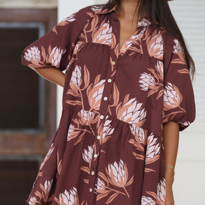 woman wearing brown button up puffy sleeve baby doll dress with protea pattern