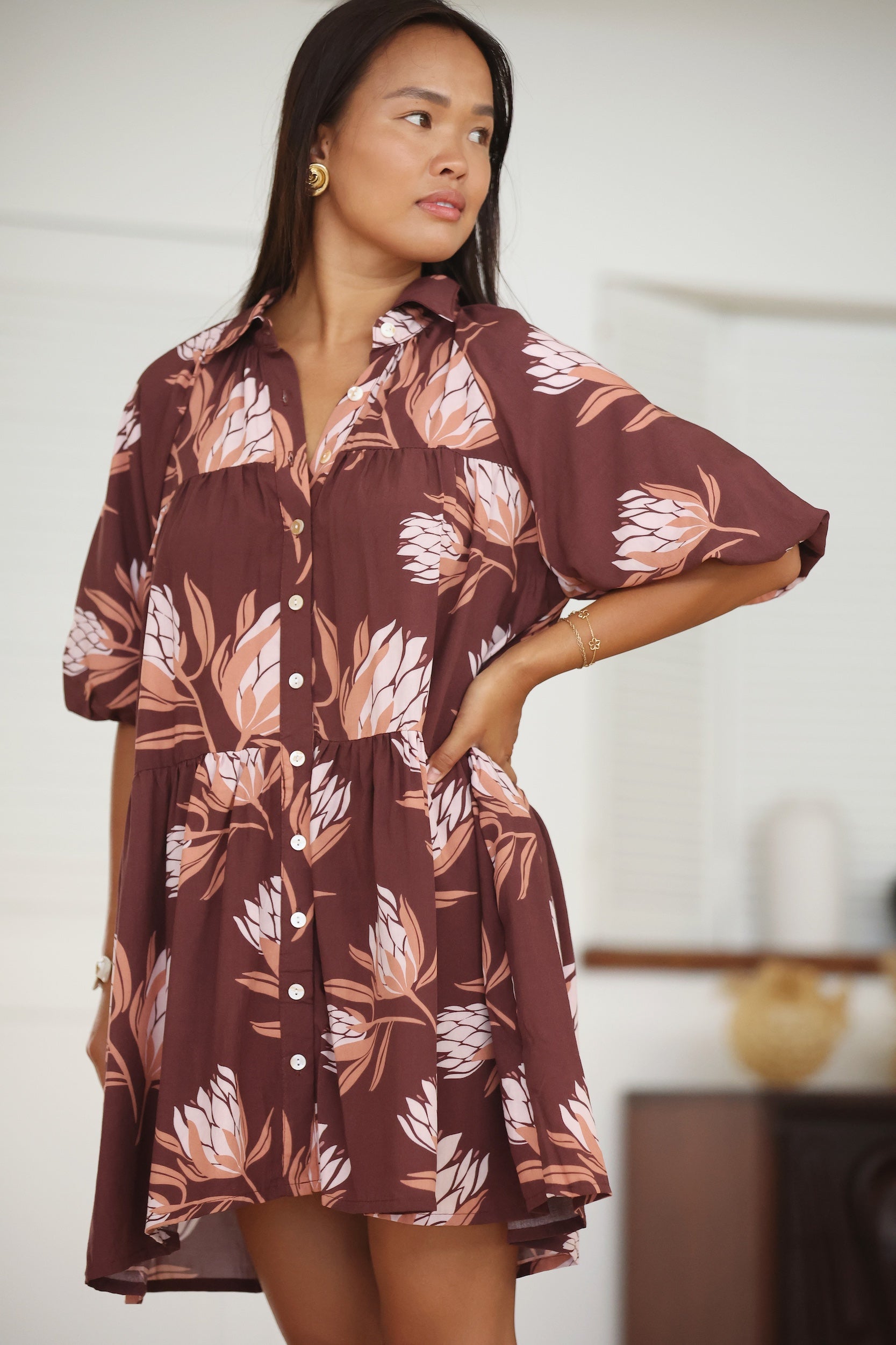 woman wearing brown button up puffy sleeve baby doll dress with protea pattern