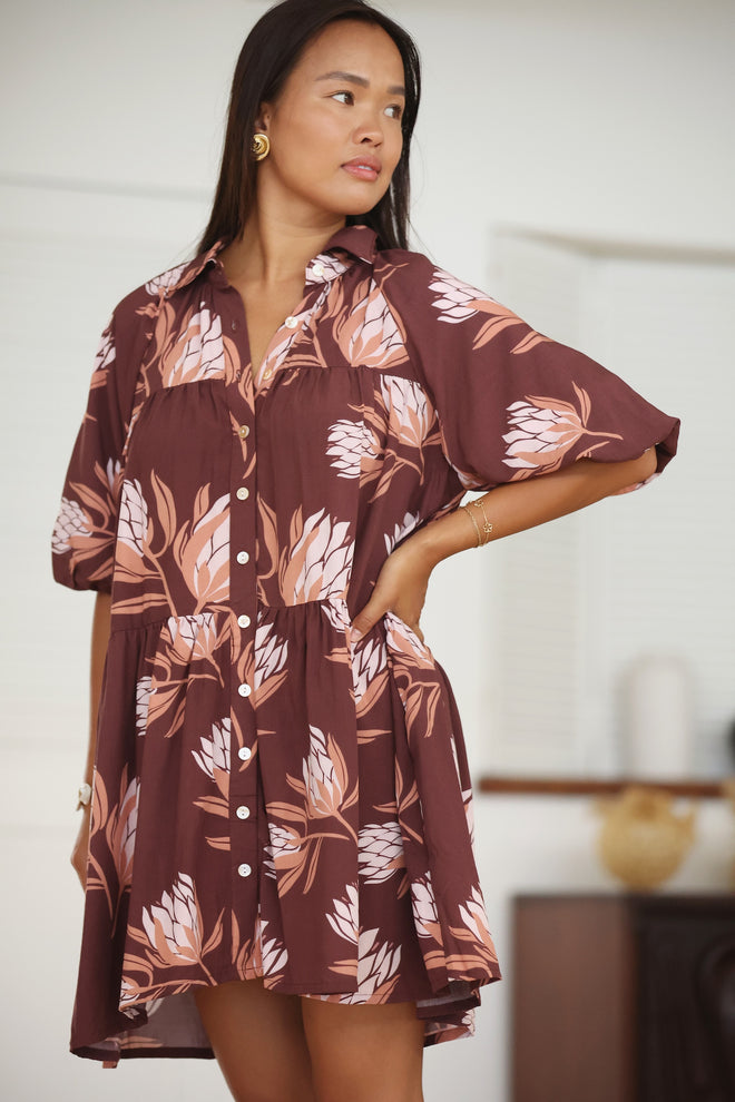 woman wearing brown button up puffy sleeve baby doll dress with protea pattern