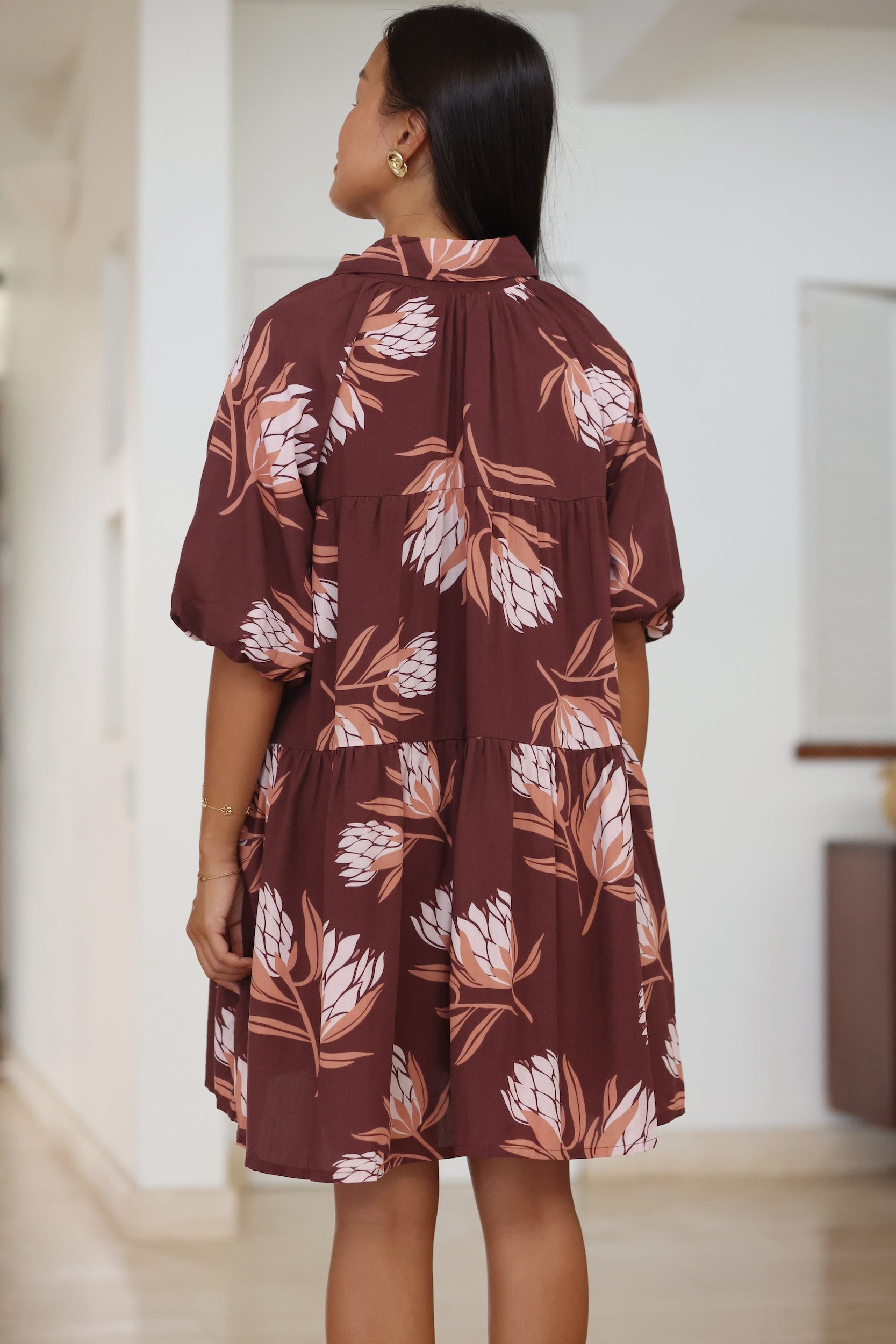 woman wearing brown button up puffy sleeve baby doll dress with protea pattern