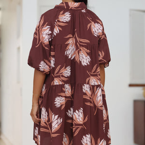 woman wearing brown button up puffy sleeve baby doll dress with protea pattern