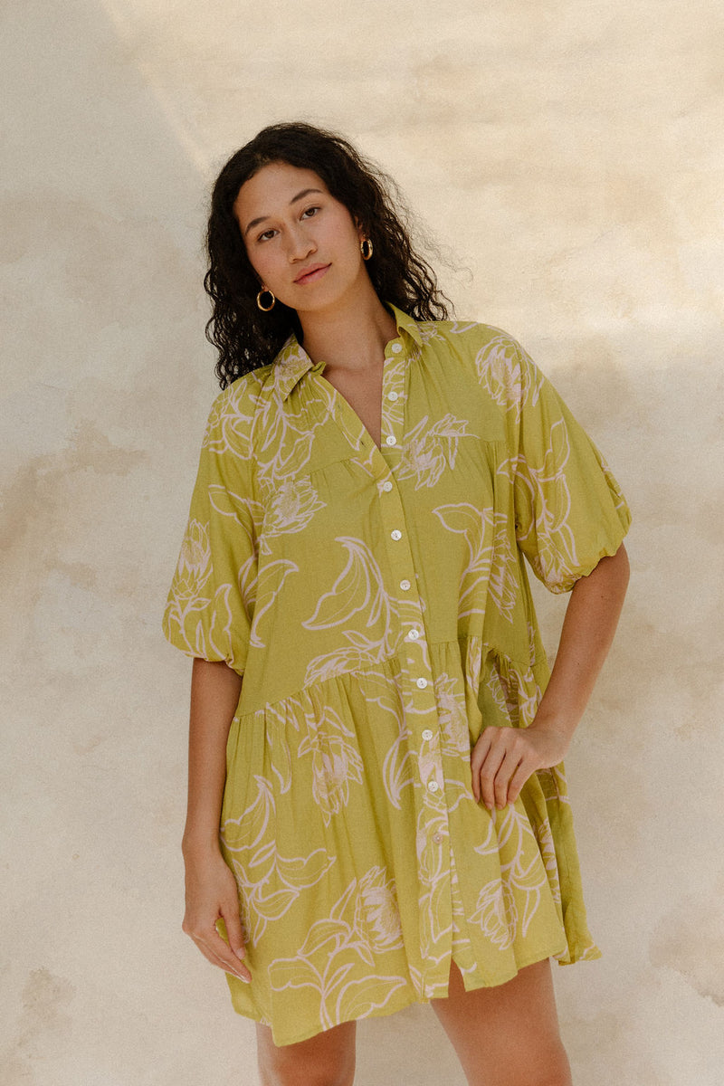 Woman in flowy short sleeve shirt dress with light green and beige floral print.