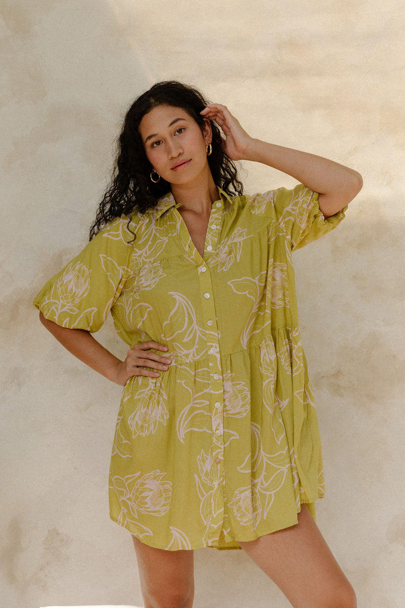 Woman in flowy short sleeve shirt dress with light green and beige floral print.