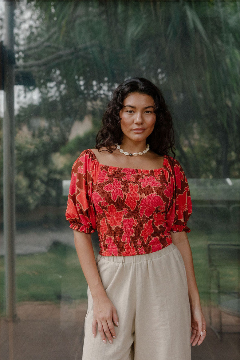 woman wearing versatile smocked top with off the shoulder on the shoulder sleeves in a vibrant retro pink pua print