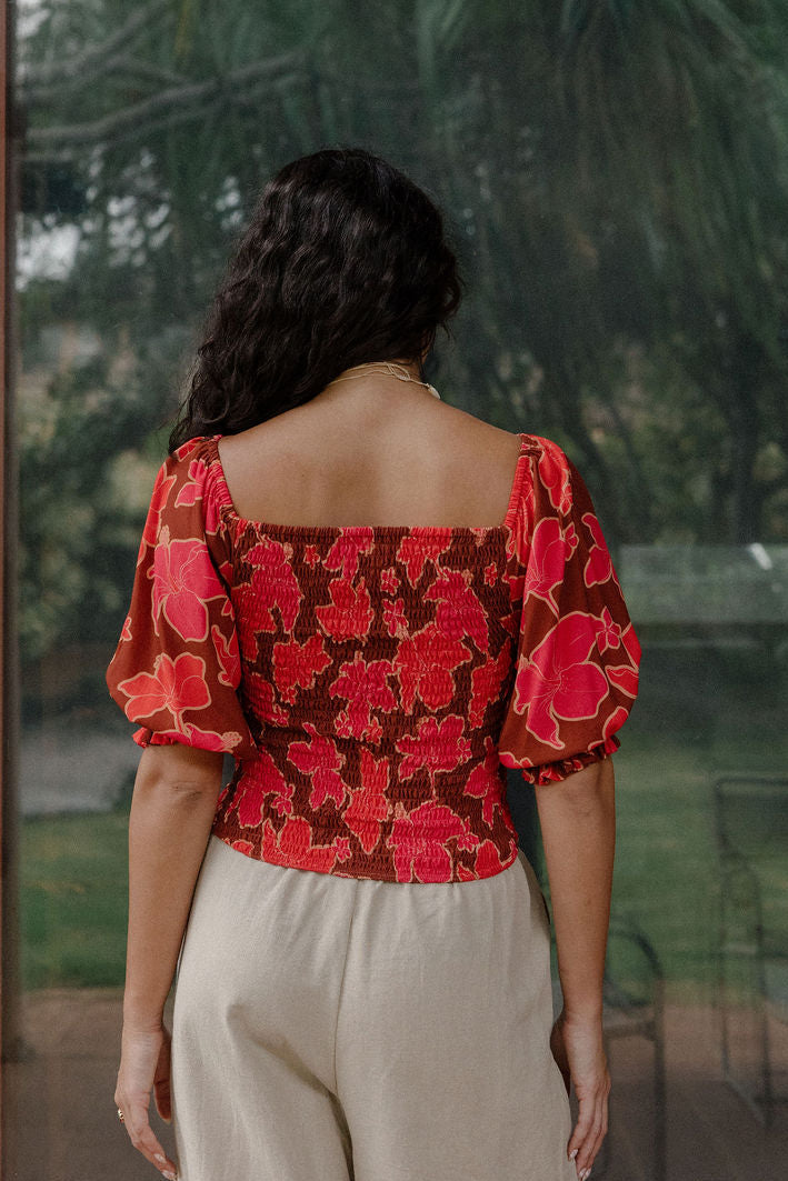 woman wearing versatile smocked top with off the shoulder on the shoulder sleeves in a vibrant retro pink pua print