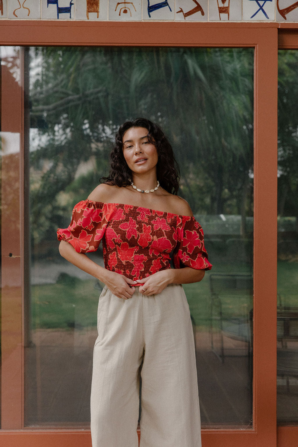 woman wearing versatile smocked top with off the shoulder on the shoulder sleeves in a vibrant retro pink pua print
