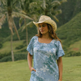 woman with brown hair wearing a blue paniolo printed mu'u style dress with flutter sleeves and a ruffle hem 