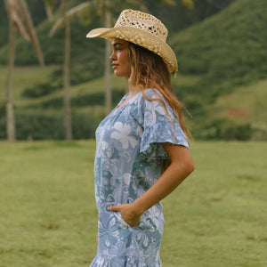 woman with brown hair wearing a blue paniolo printed mu'u style dress with flutter sleeves and a ruffle hem 