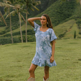 woman with brown hair wearing a blue paniolo printed mu'u style dress with flutter sleeves and a ruffle hem 