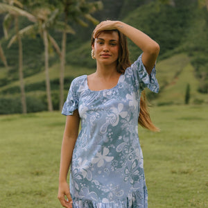woman with brown hair wearing a blue paniolo printed mu'u style dress with flutter sleeves and a ruffle hem 
