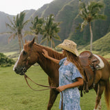 woman with brown hair wearing a blue paniolo printed mu'u style dress with flutter sleeves and a ruffle hem 