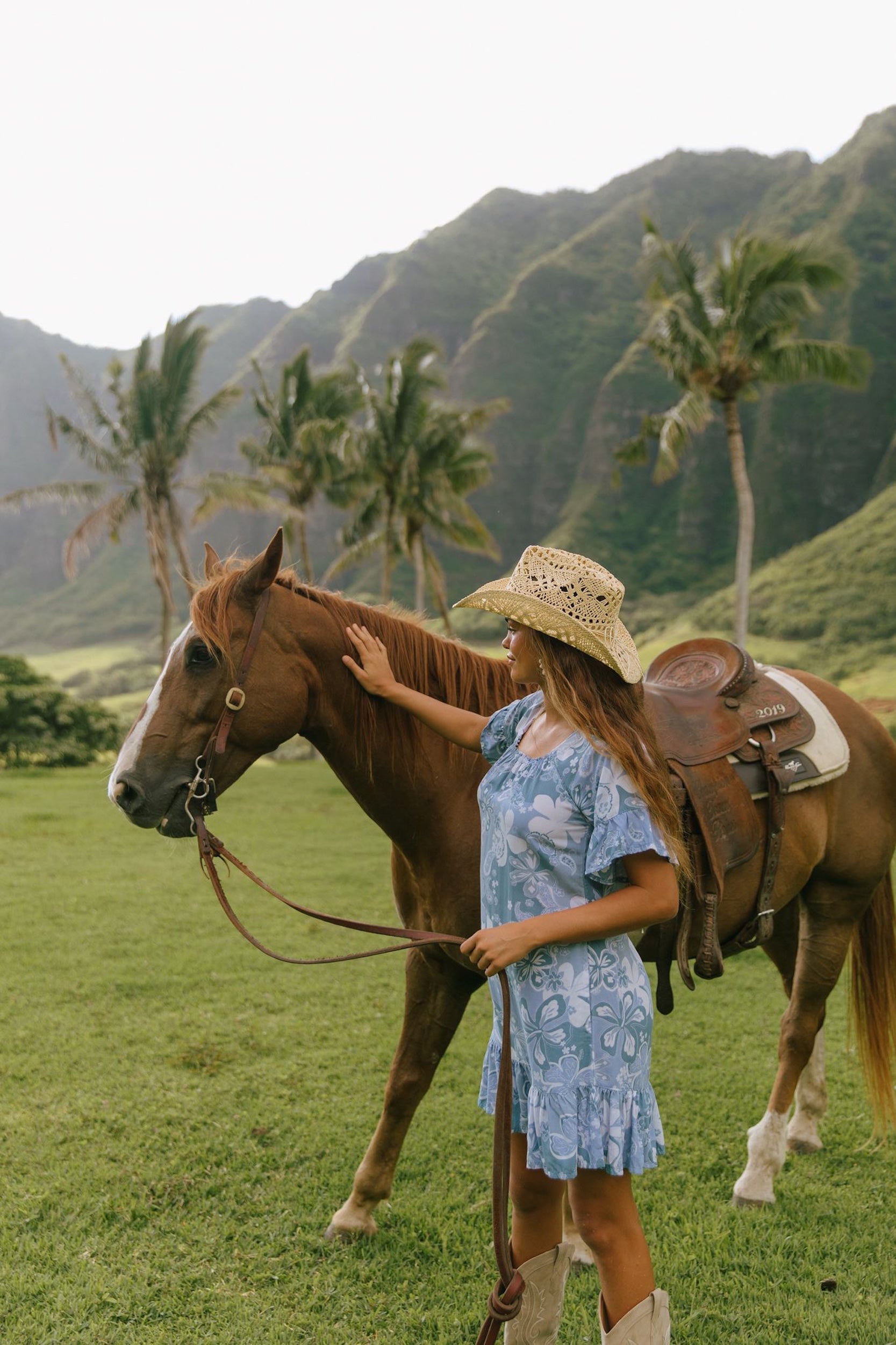 woman with brown hair wearing a blue paniolo printed mu'u style dress with flutter sleeves and a ruffle hem 