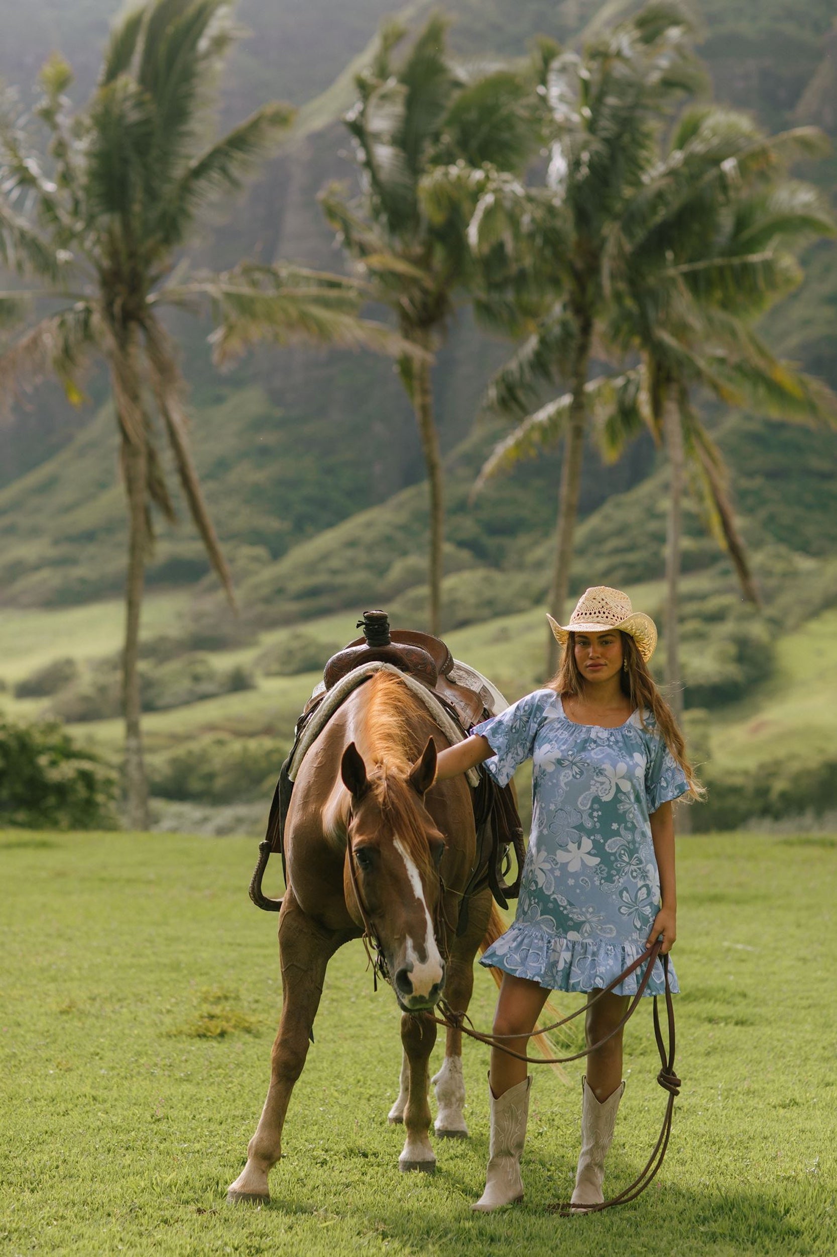 woman with brown hair wearing a blue paniolo printed mu'u style dress with flutter sleeves and a ruffle hem 