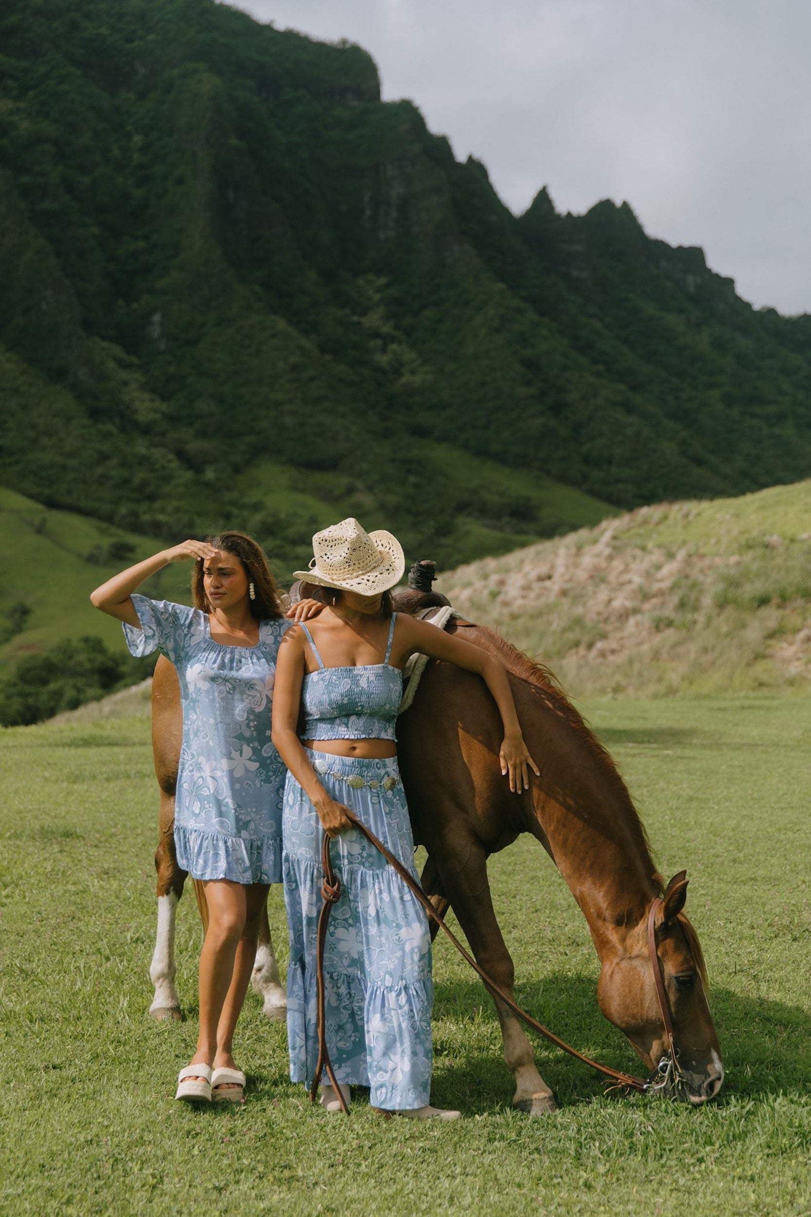 woman with brown hair wearing a blue paniolo printed mu'u style dress with flutter sleeves and a ruffle hem 