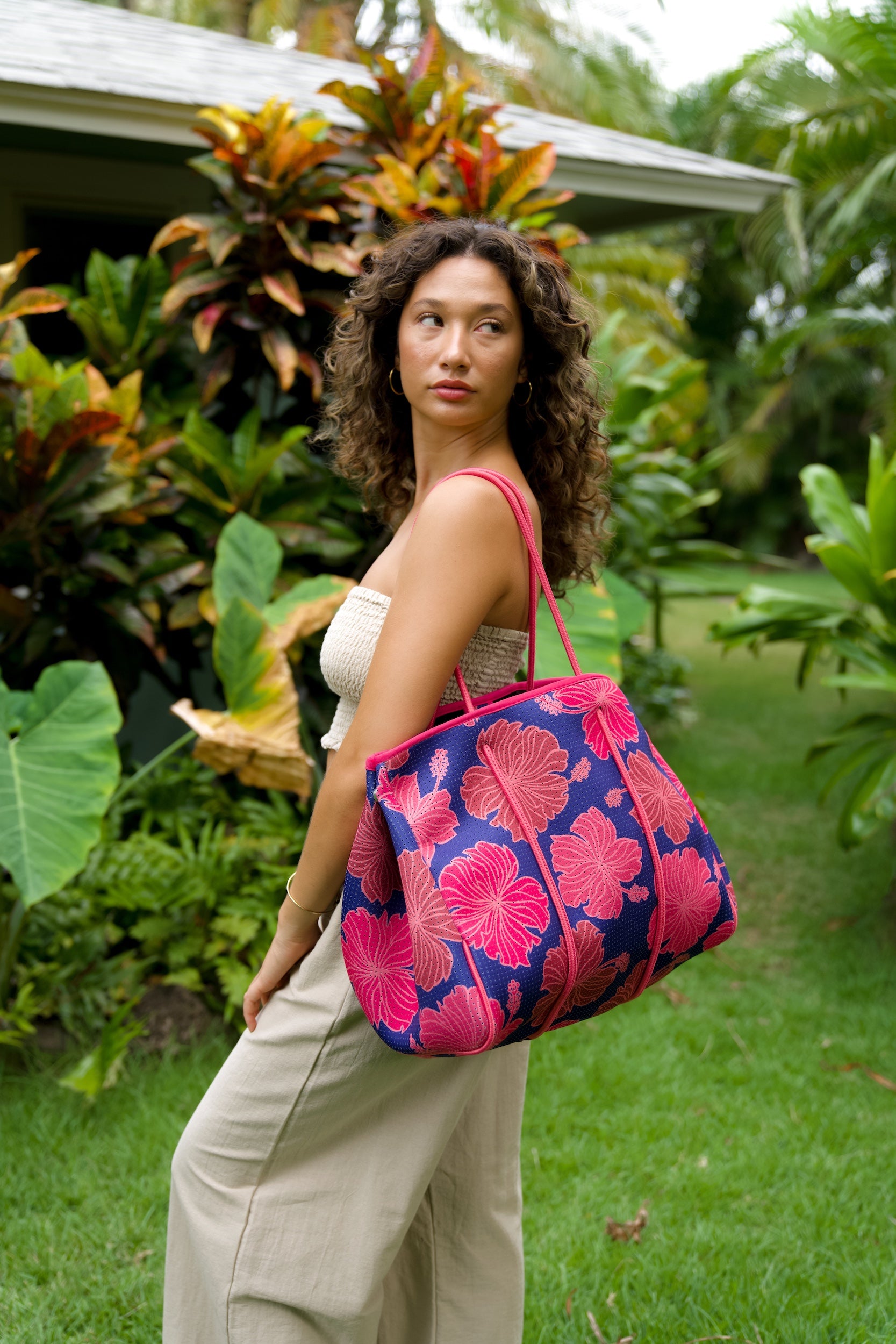 woman carrying large dark navy blue everyday tote bag with rope straps, detachable mini pouch, and bright pink hibiscus print