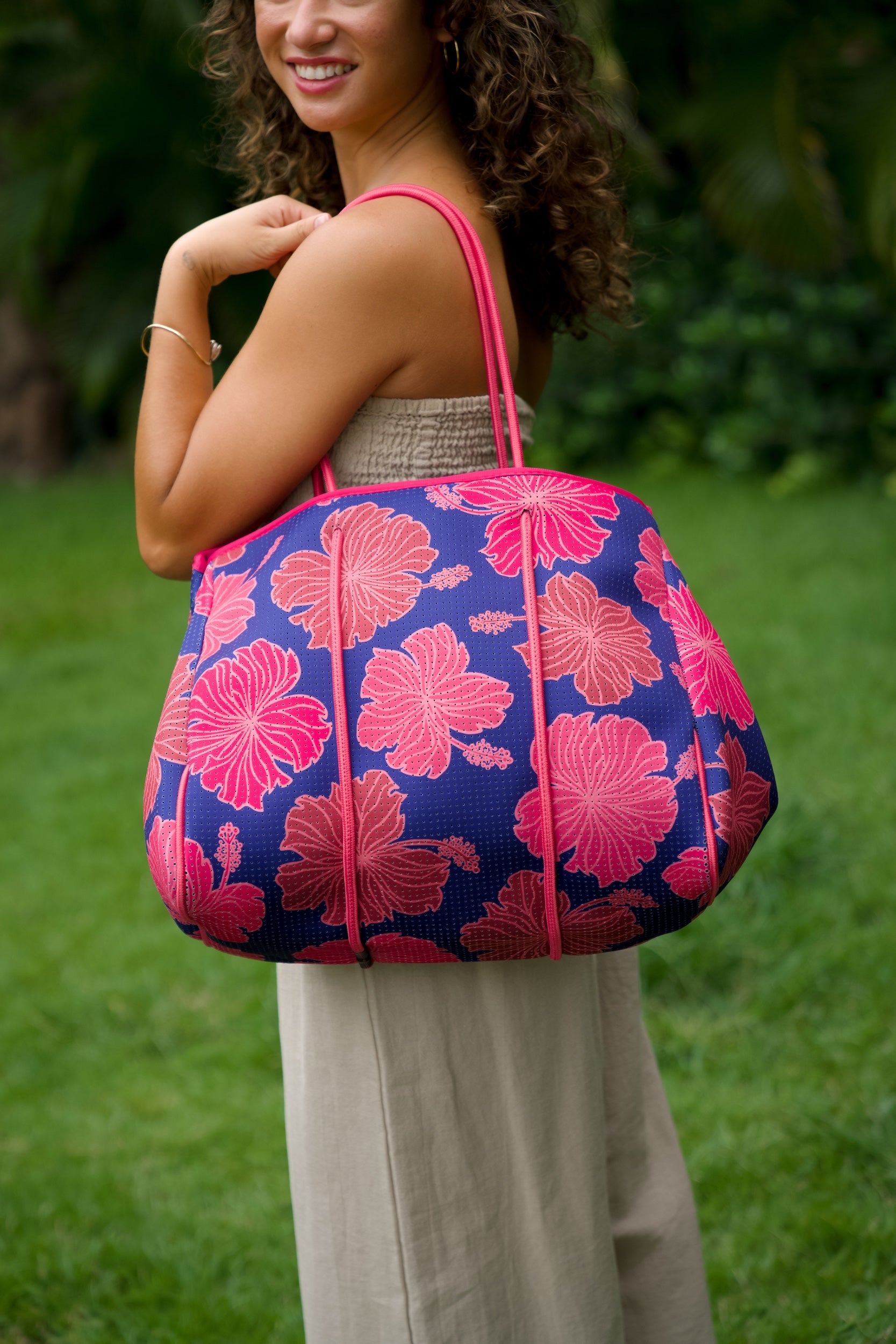woman carrying large dark navy blue everyday tote bag with rope straps, detachable mini pouch, and bright pink hibiscus print