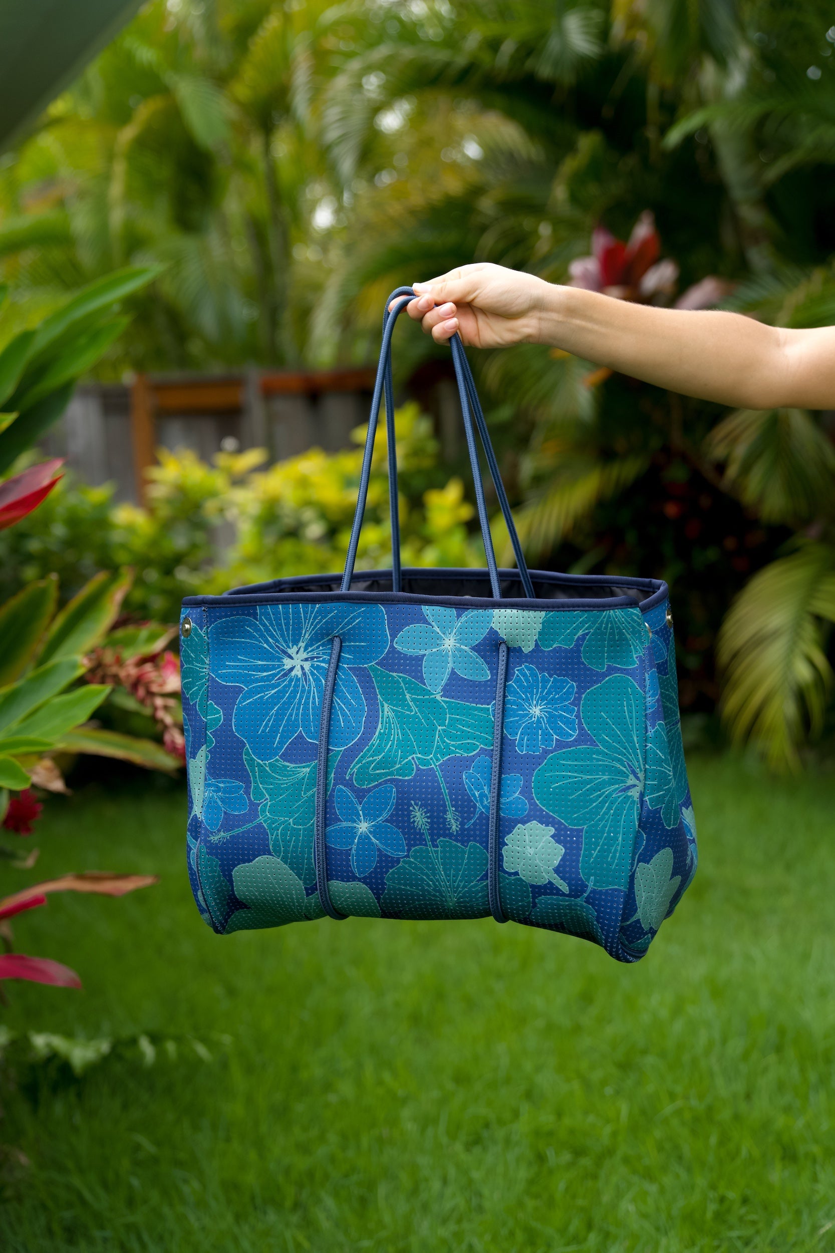 woman carrying large dark navy blue everyday tote bag with rope straps, detachable mini pouch, and blue/green flower print
