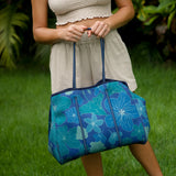 woman carrying large dark navy blue everyday tote bag with rope straps, detachable mini pouch, and blue/green flower print
