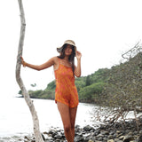 woman with brown hair wearing an orange overall style romper with rumi bandeau underneath with puakenikeni print
