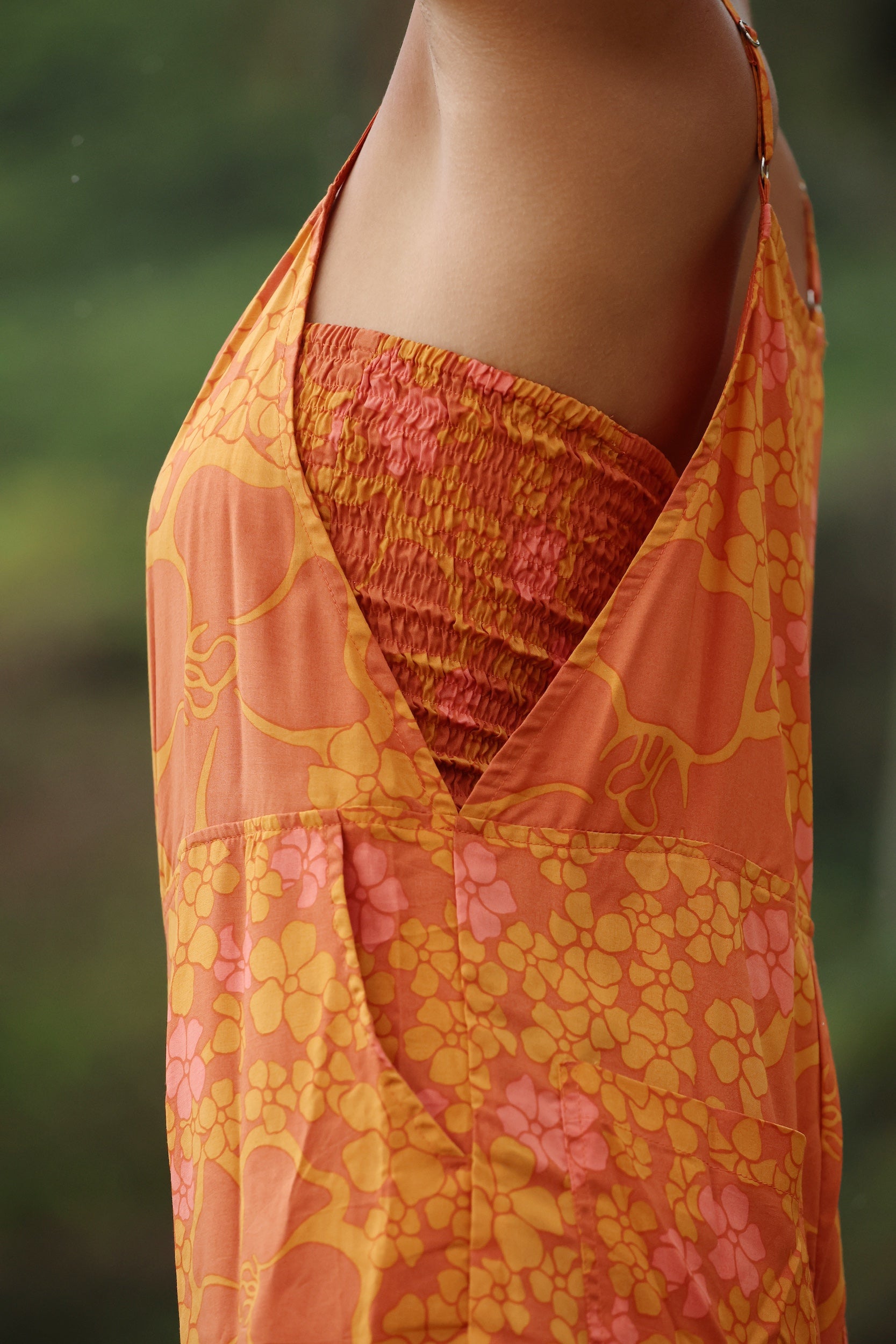woman with brown hair wearing an orange overall style romper with rumi bandeau underneath with puakenikeni print