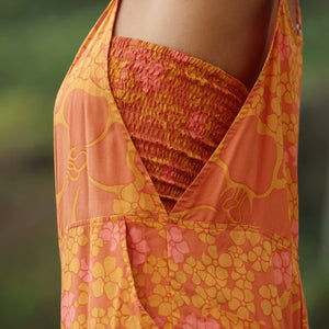 woman with brown hair wearing an orange overall style romper with rumi bandeau underneath with puakenikeni print